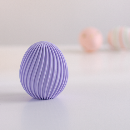 Œuf de Pâques décoratif strié violet pastel imprimé en 3D posé sur fond clair