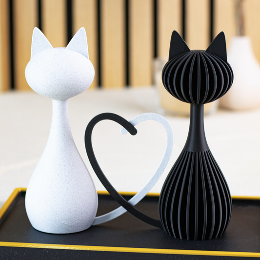 Duo de statuettes de chats amoureux formant un cœur avec leurs queues, finition marbre blanc lisse et noir mat rainuré, posés sur un plateau décoratif.